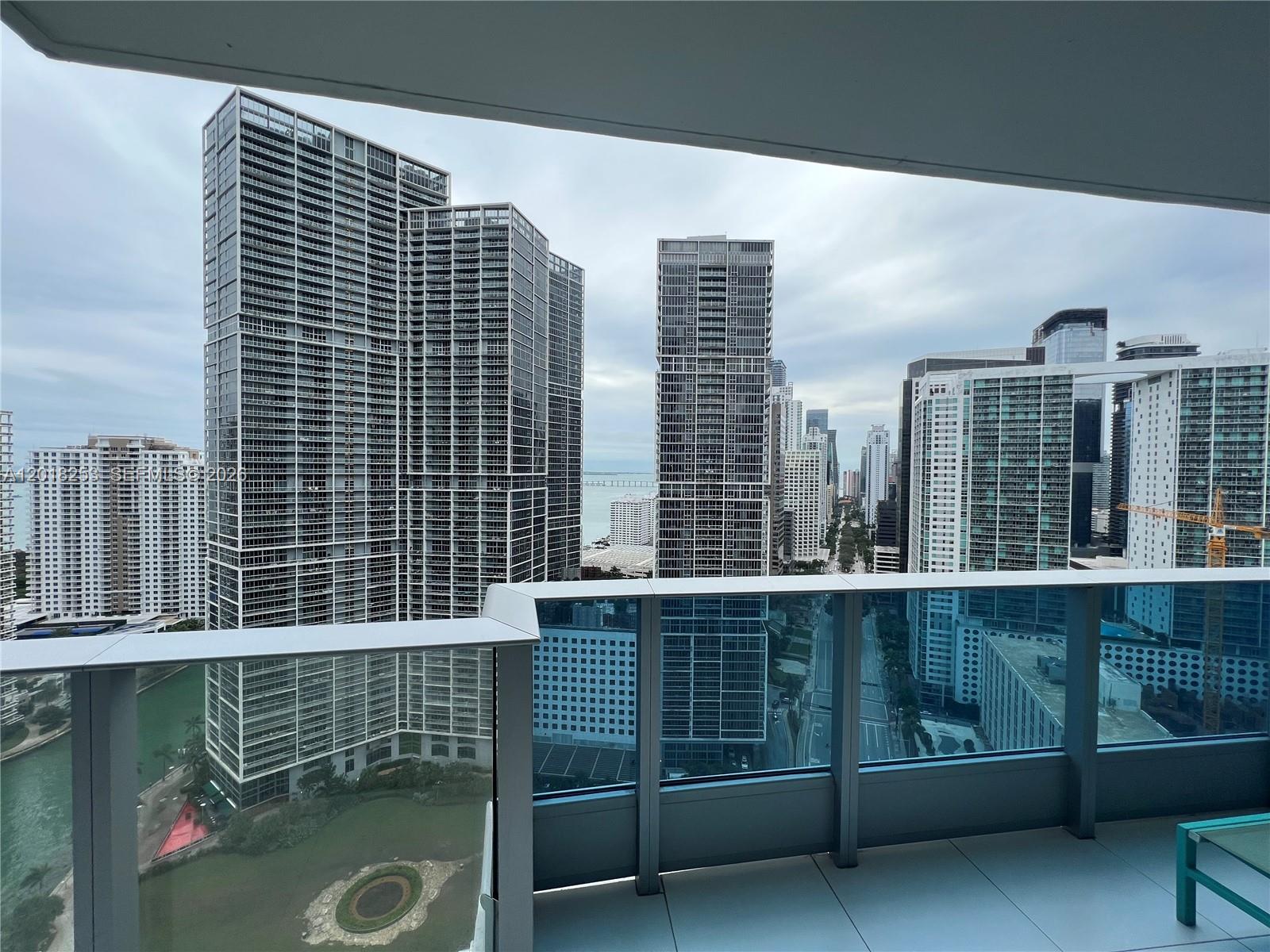 A balcony view overlooking a city skyline with multiple high-rise buildings and a body of water — 200 Biscayne Boulevard Way # 3106, Miami FL 33131, MIAMI, FL