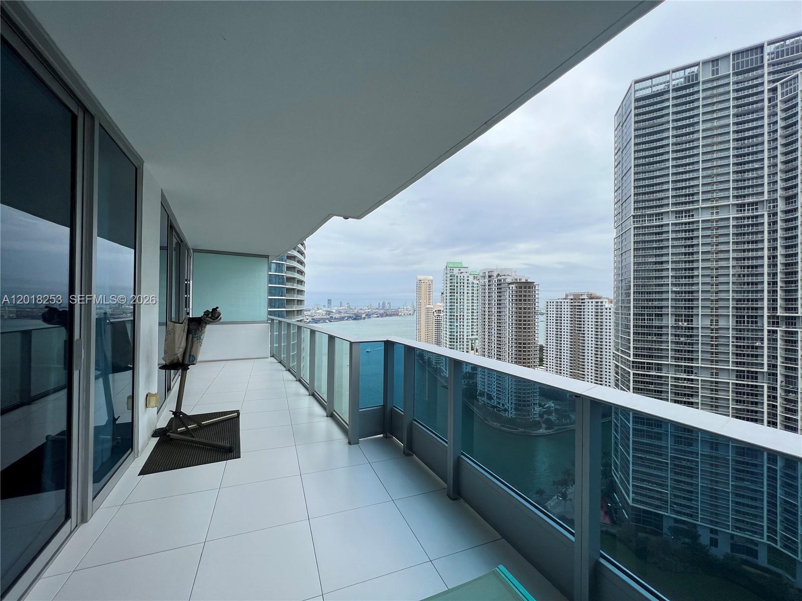 A balcony with white tile flooring overlooks a city skyline and a body of water — 200 Biscayne Boulevard Way # 3106, Miami FL 33131, MIAMI, FL