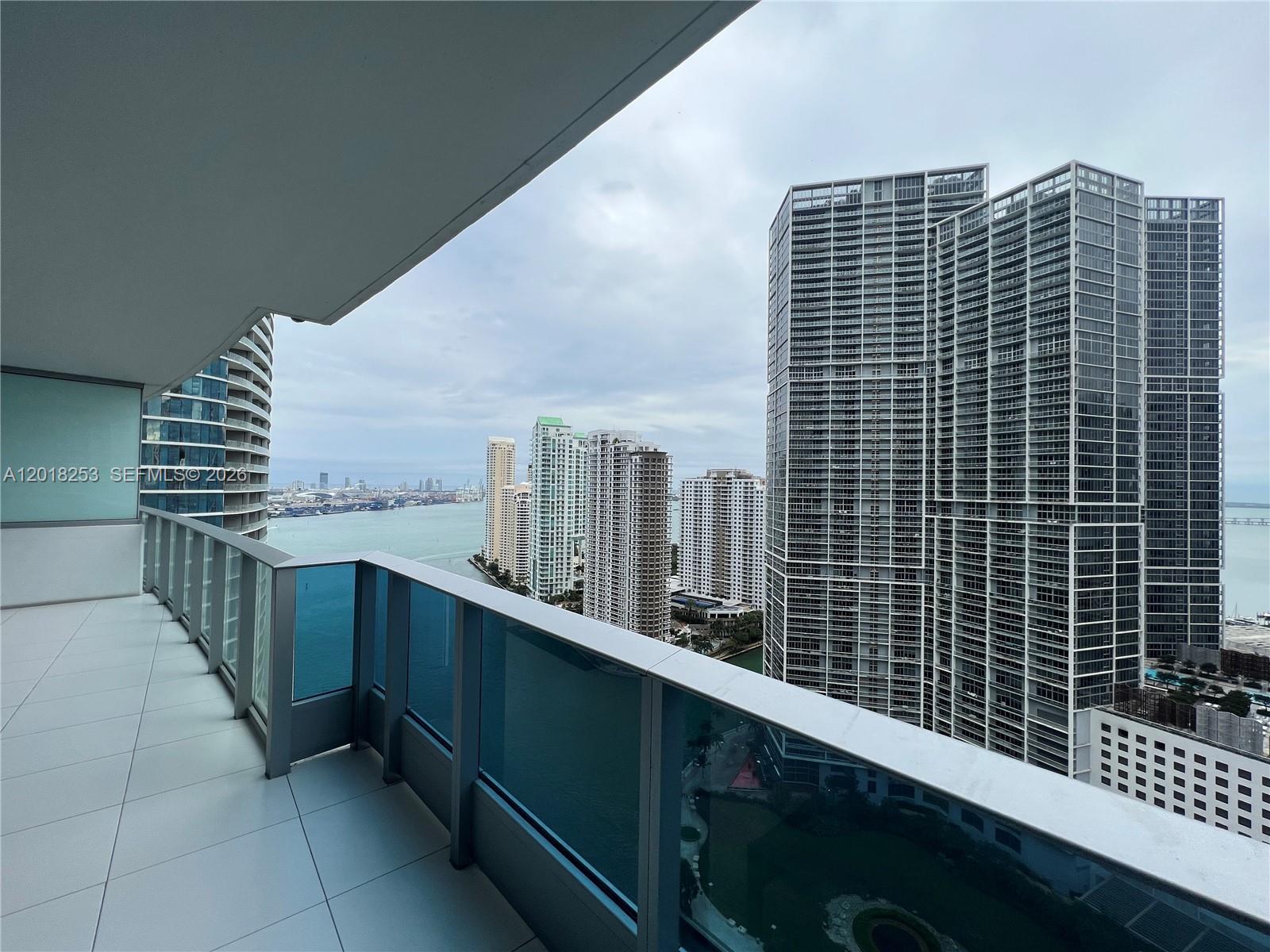 A balcony with glass railings overlooks a bay and a dense city skyline — 200 Biscayne Boulevard Way # 3106, Miami FL 33131, MIAMI, FL