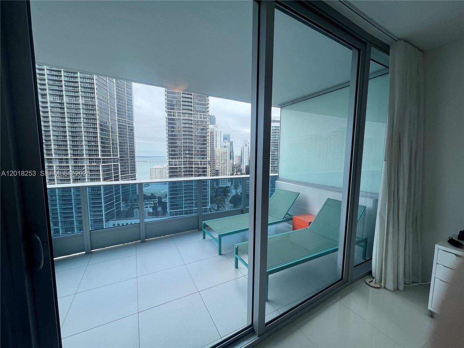 A balcony with two lounge chairs overlooks a city skyline and a body of water — 200 Biscayne Boulevard Way # 3106, Miami FL 33131, MIAMI, FL