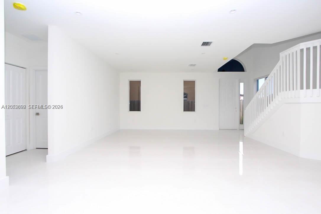 A bright, empty room features white walls, glossy tile flooring, and a white staircase — 15631 SW 11th Ter, Miami FL 33194, MIAMI, FL