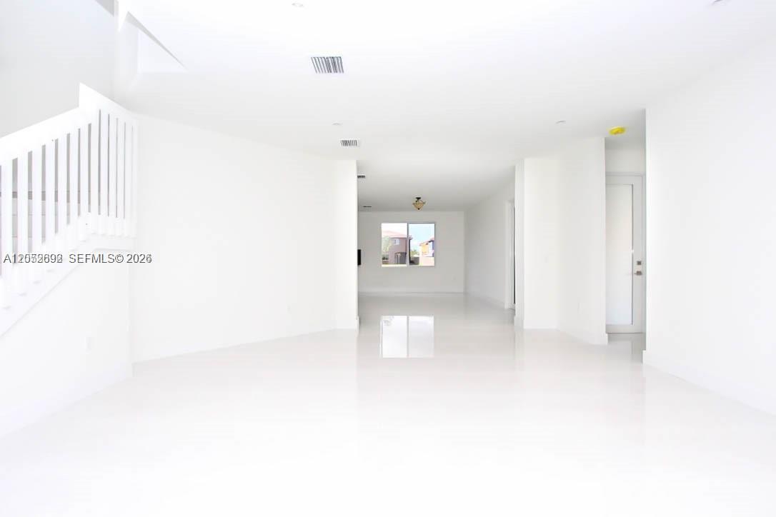 An empty, white-walled living area features glossy tile flooring and a staircase on the left — 15631 SW 11th Ter, Miami FL 33194, MIAMI, FL