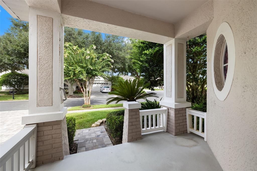A covered front porch features stucco columns, brick bases, white railings, and a circular window — 19425 MELODY FAIR PLACE, LUTZ, FL