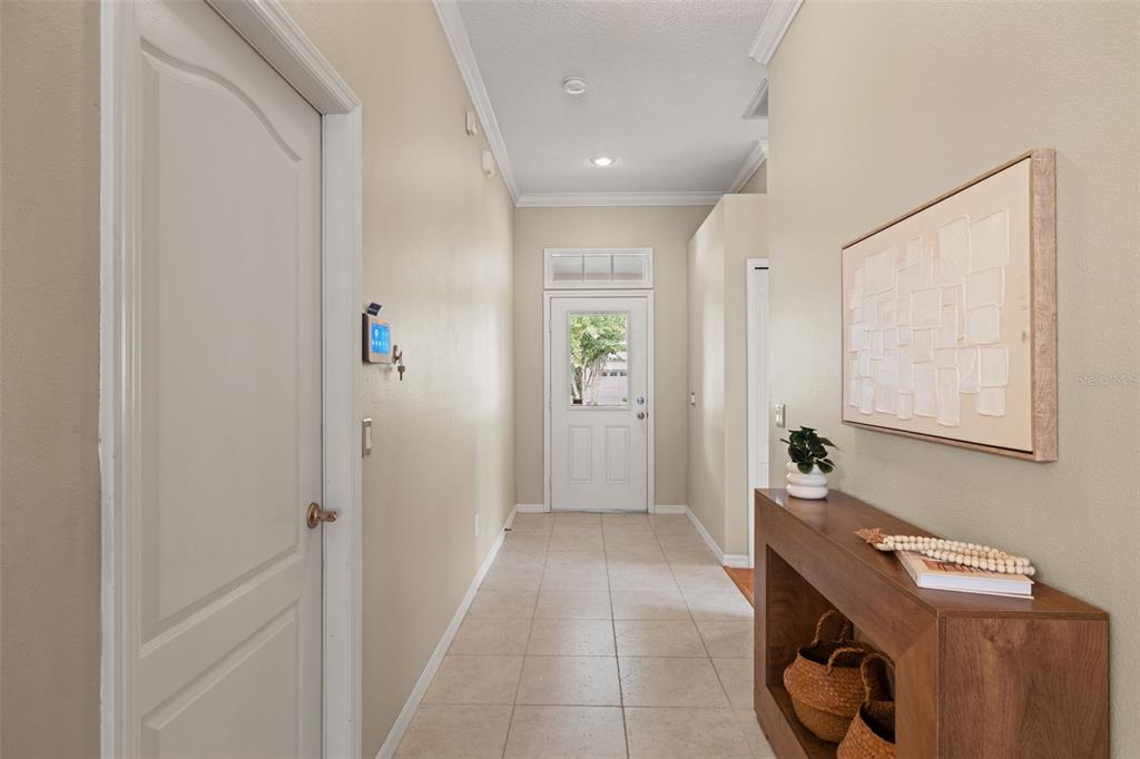 A hallway with beige tile floors leads to a white front door with a window — 19425 MELODY FAIR PLACE, LUTZ, FL