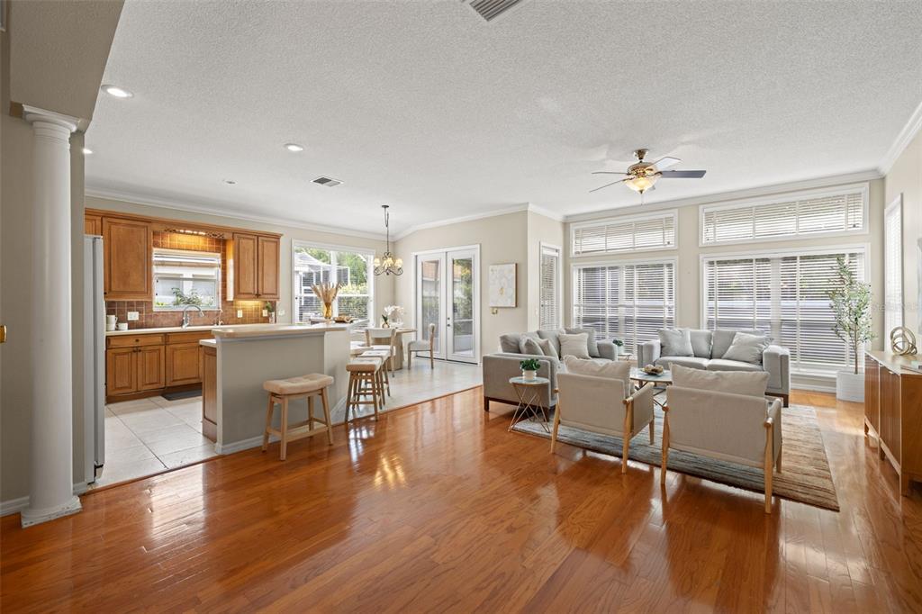 An open-concept living area features hardwood floors, a kitchen with wood cabinets, and large windows — 19425 MELODY FAIR PLACE, LUTZ, FL