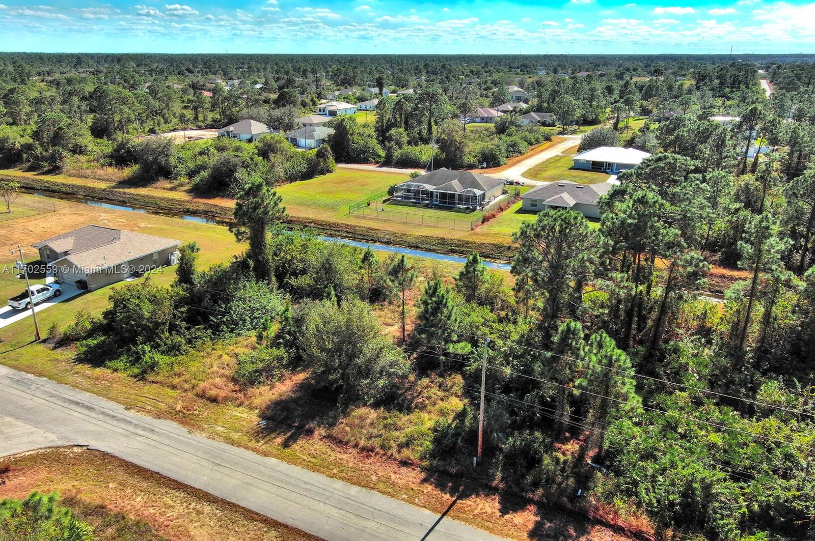 An aerial view shows a residential neighborhood with houses, a canal, and wooded lots — 844 Carbon St E, Lehigh Acres FL 33974, LEHIGH ACRES, FL