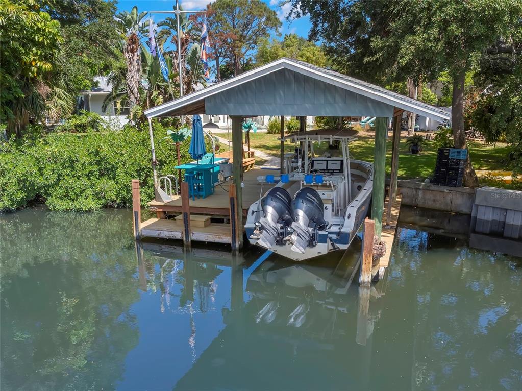 A boat with twin outboard motors is docked under a covered lift on a canal — 121 CARLYLE DRIVE, PALM HARBOR, FL