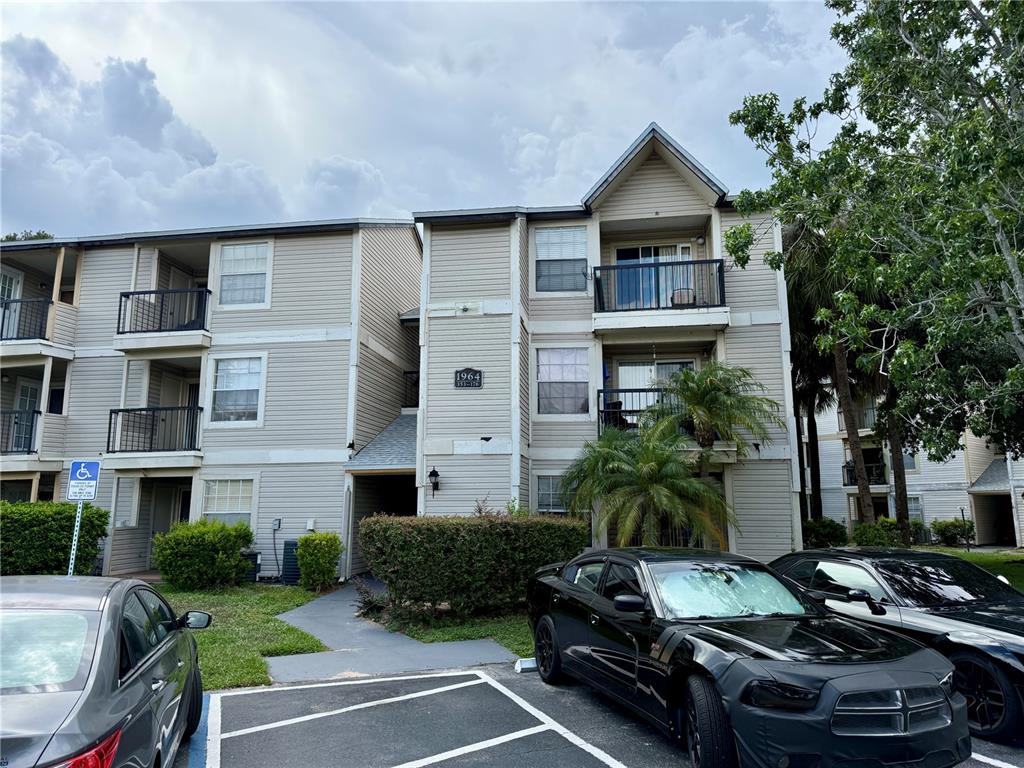 A three-story apartment building with beige siding and balconies stands behind a parking lot — 1964 LAKE ATRIUMS CIRCLE UNIT 171, ORLANDO, FL