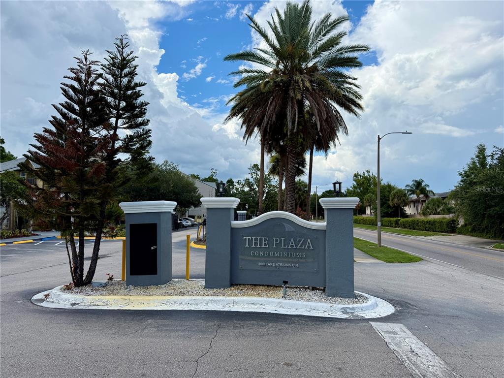 A gray monument sign for The Plaza Condominiums stands at an entrance with palm trees — 1964 LAKE ATRIUMS CIRCLE UNIT 171, ORLANDO, FL