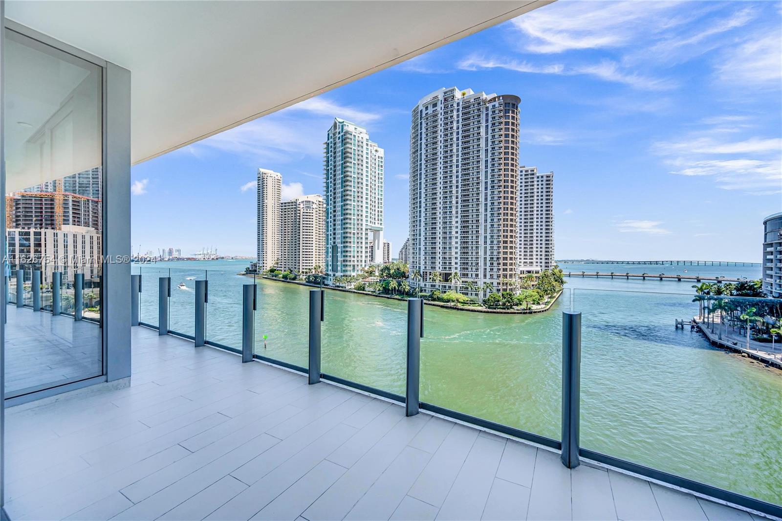 A balcony with a glass railing overlooks a bay and high-rise buildings in Miami — 300 Biscayne Blvd Way # 703, Miami FL 33131, MIAMI, FL