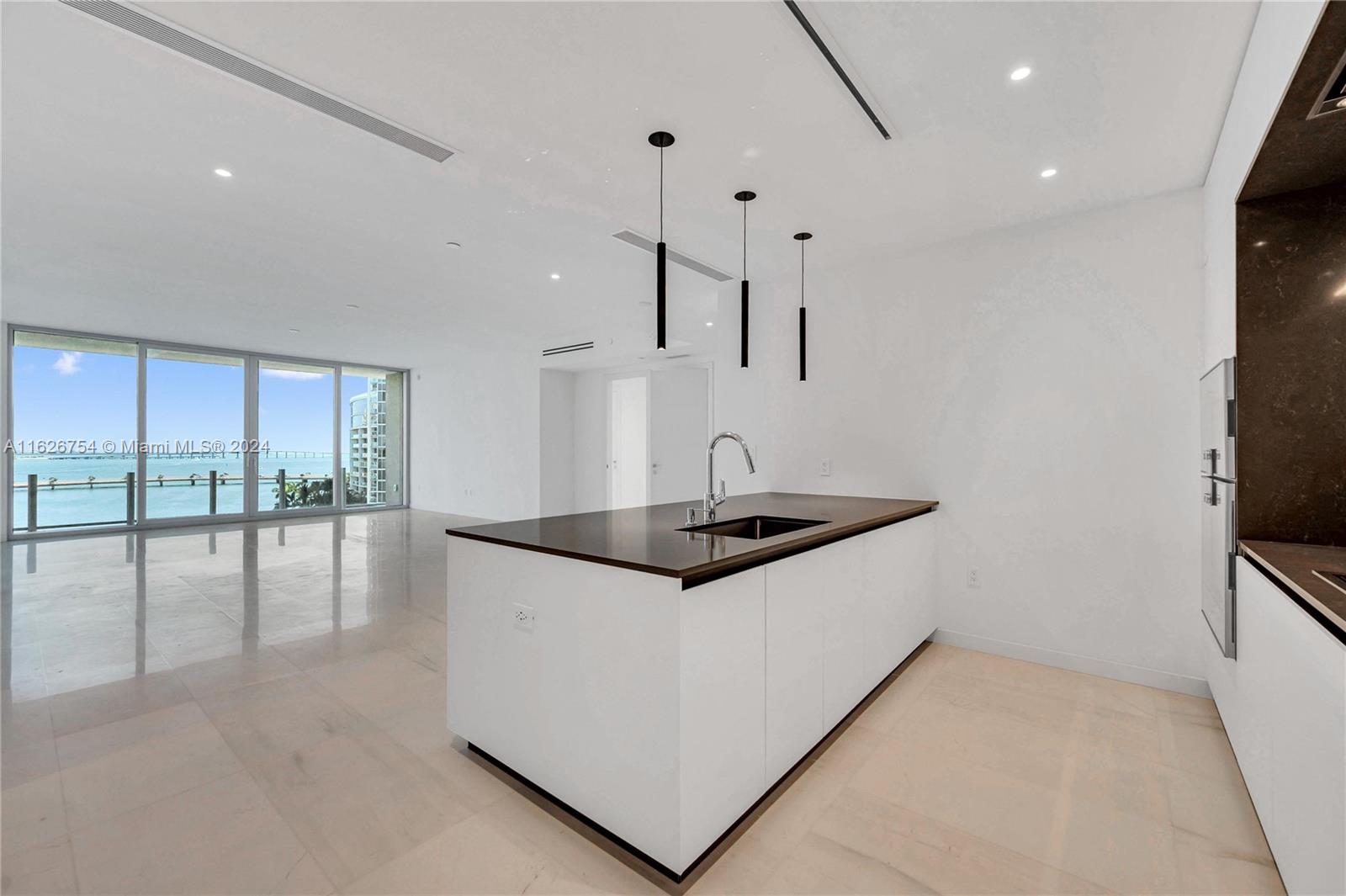 A modern kitchen features a white island with a dark countertop and ocean views — 300 Biscayne Blvd Way # 703, Miami FL 33131, MIAMI, FL