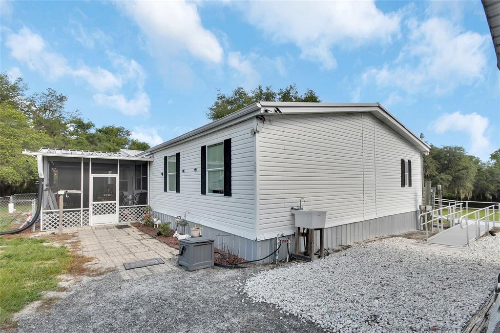 A light-colored mobile home features a screened-in porch, a gravel driveway, and a wheelchair ramp — 38846 FOREST DRIVE, EUSTIS, FL