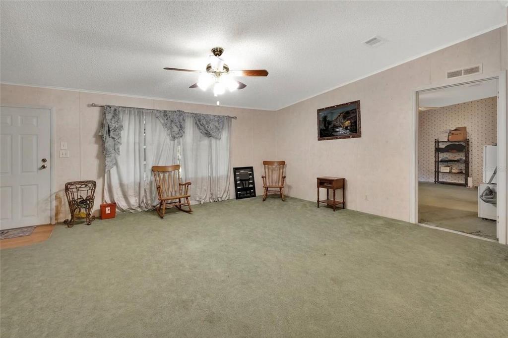A living room features green carpeting, light-colored walls, a ceiling fan, and two wooden rockers — 38846 FOREST DRIVE, EUSTIS, FL