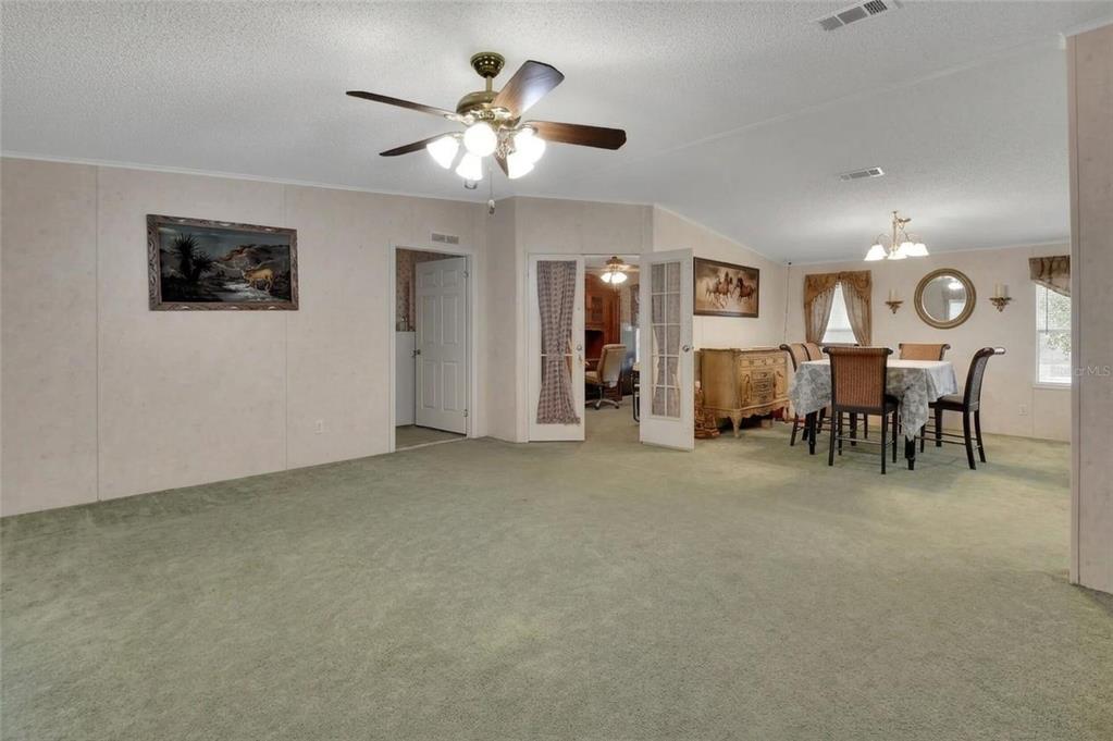 A spacious living room with green carpet, a ceiling fan, and an adjacent dining area — 38846 FOREST DRIVE, EUSTIS, FL