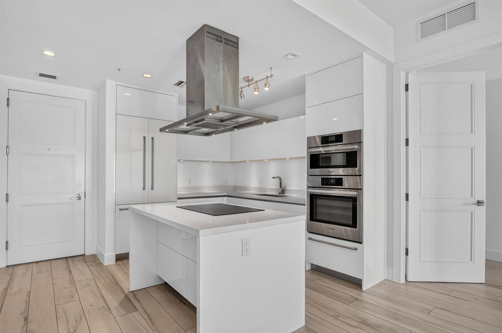 A modern kitchen features white cabinetry, stainless steel appliances, a central island, and wood flooring — 155 E Boca Raton Road # 1019, Boca Raton FL 33432, BOCA RATON, FL