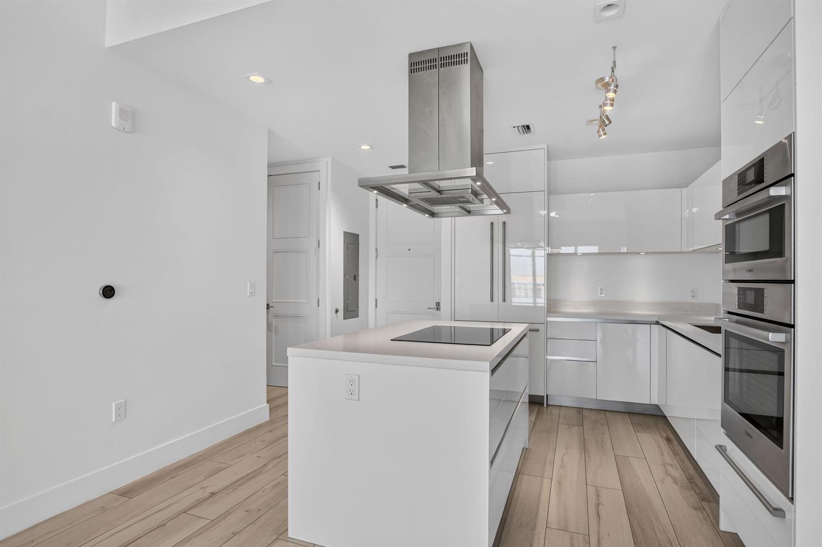 A modern kitchen features white cabinetry, a central island with a cooktop, and wood-look flooring — 155 E Boca Raton Road # 1019, Boca Raton FL 33432, BOCA RATON, FL