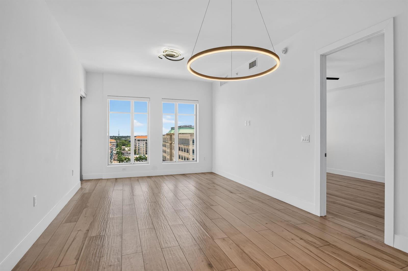 An empty room with light wood floors, white walls, a circular chandelier, and city views — 155 E Boca Raton Road # 1019, Boca Raton FL 33432, BOCA RATON, FL