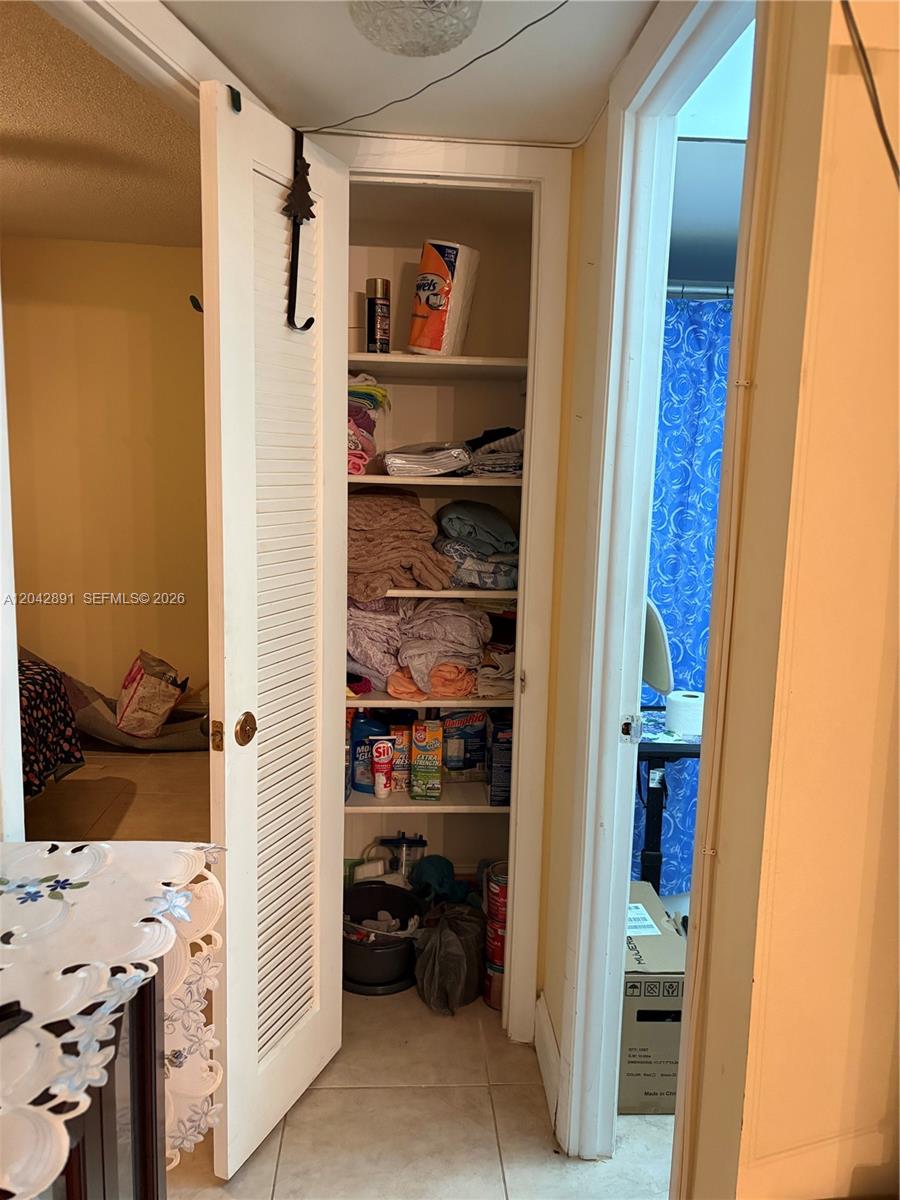 A hallway closet with open louvered doors reveals shelves filled with linens and household supplies — 2741 N Pine Island Rd # 109, Sunrise FL 33322, SUNRISE, FL