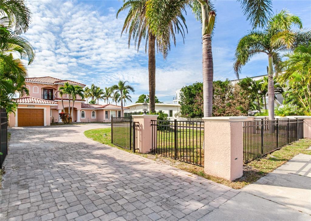 A two-story pink house with a paved driveway and palm trees behind a metal fence — 16116 GULF BOULEVARD, REDINGTON BEACH, FL