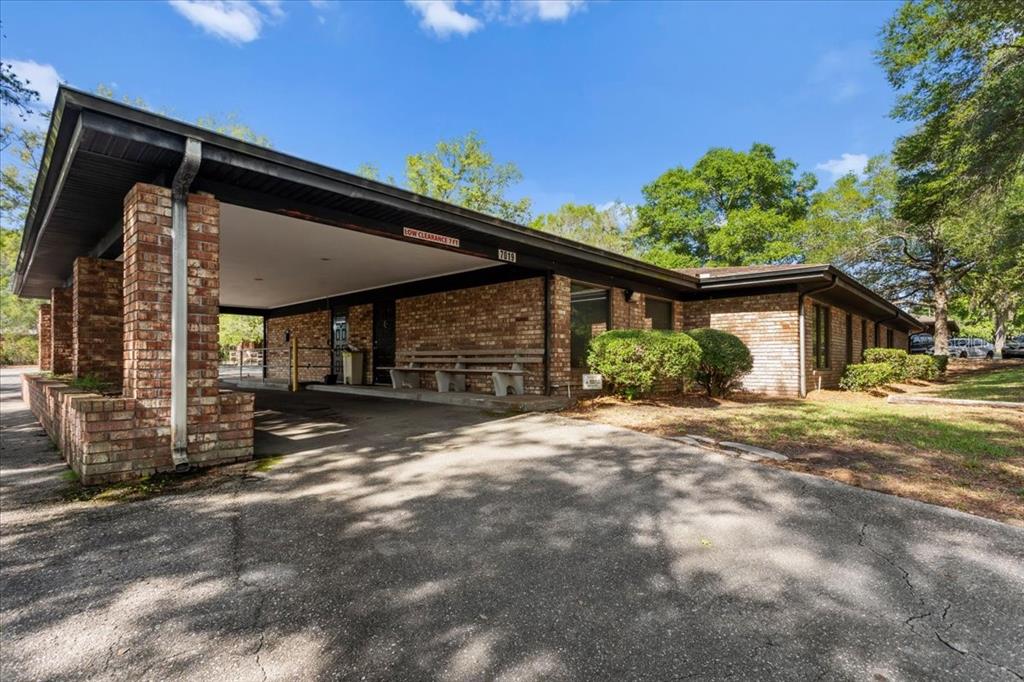 A single-story brick building features a large covered carport area and a concrete driveway — 7019 NW 11TH PLACE, GAINESVILLE, FL