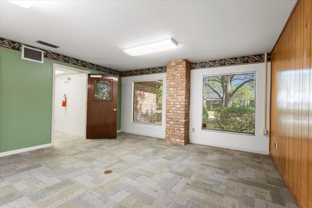 An office room features green walls, wood paneling, a brick pillar, and patterned carpet flooring — 7019 NW 11TH PLACE, GAINESVILLE, FL