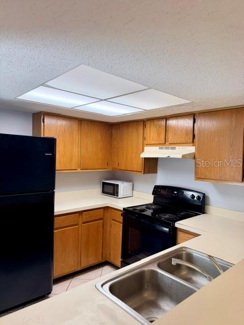 A kitchen features wood cabinets, a black refrigerator, a black stove, and a double sink — 5627 GREATPINE LANE N, JACKSONVILLE, FL