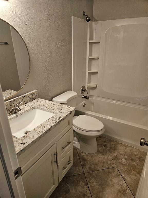 A bathroom features a granite-topped vanity, a round mirror, a toilet, and a shower-tub combo — 2744 HIDDEN LAKE BOULEVARD UNIT C, SARASOTA, FL