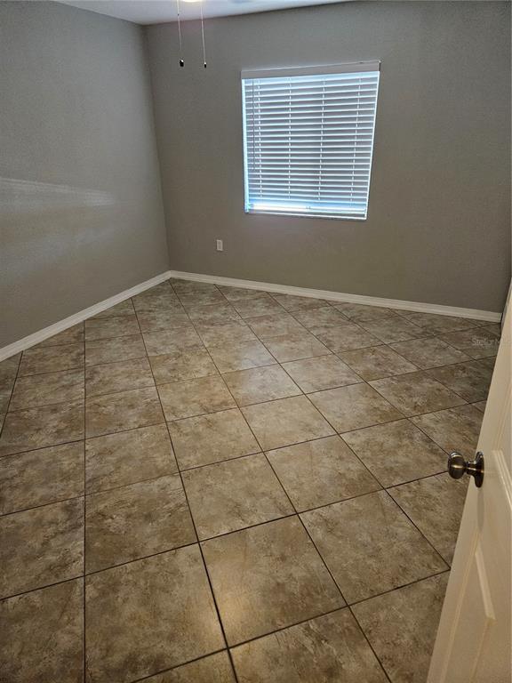 An empty room features gray walls, white baseboards, and diagonal tan tile flooring — 2744 HIDDEN LAKE BOULEVARD UNIT C, SARASOTA, FL