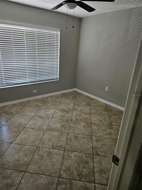 An empty room features light gray walls, a ceiling fan, and brown tiled flooring — 2744 HIDDEN LAKE BOULEVARD UNIT C, SARASOTA, FL