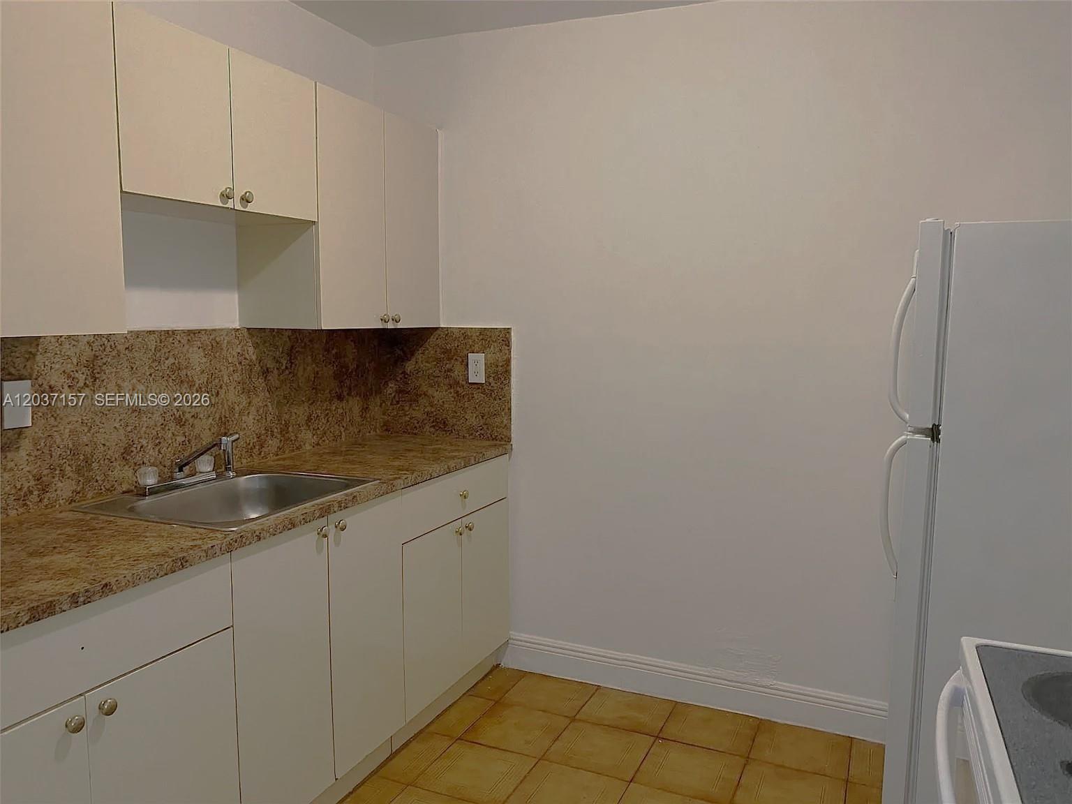 A kitchen features white cabinets, a granite countertop, a stainless steel sink, and tile flooring — 2010 NW 70th St, Miami FL 33147, MIAMI, FL