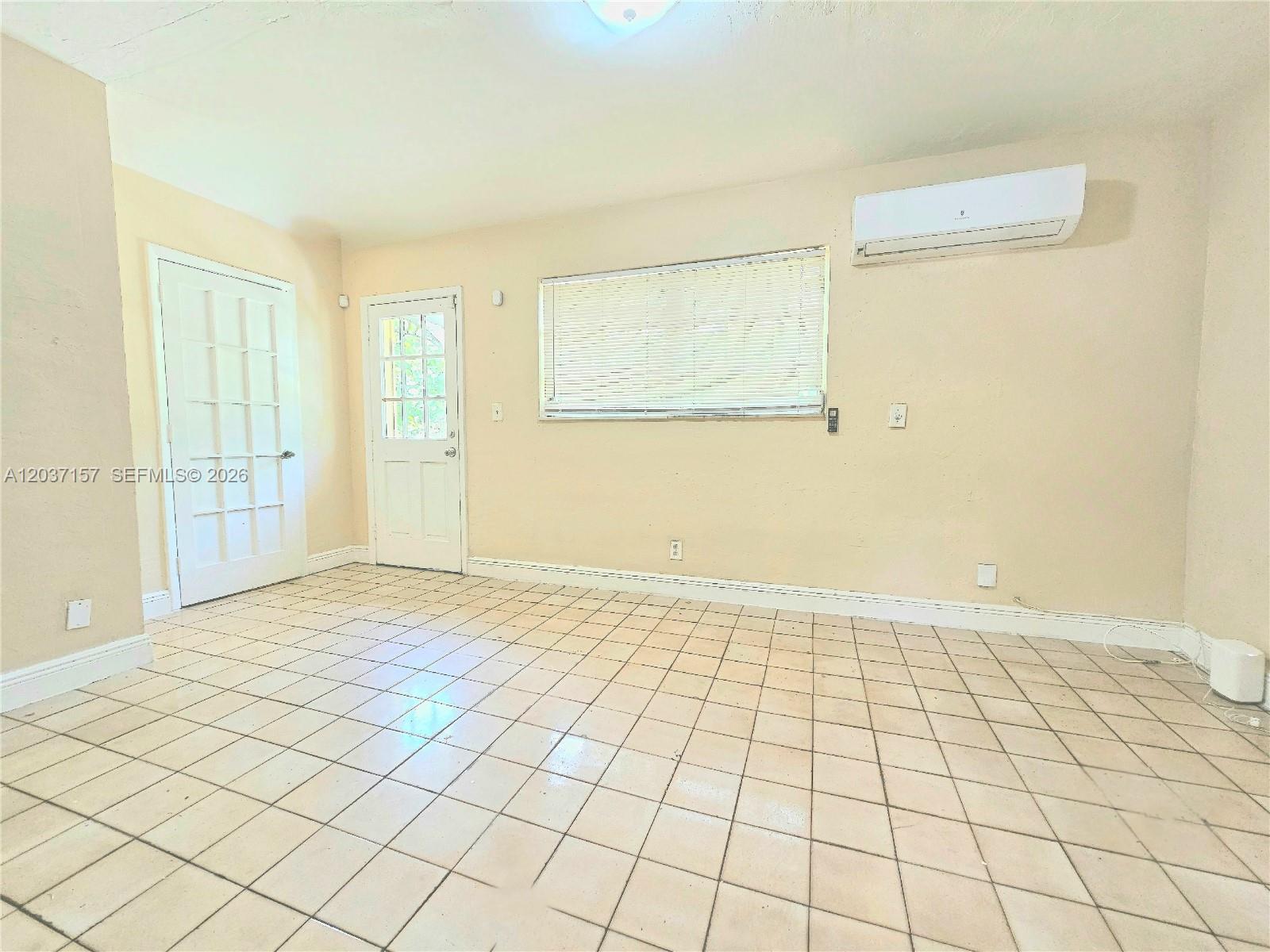 An empty room features beige walls, a tiled floor, a window, and a wall-mounted air conditioner — 2010 NW 70th St, Miami FL 33147, MIAMI, FL