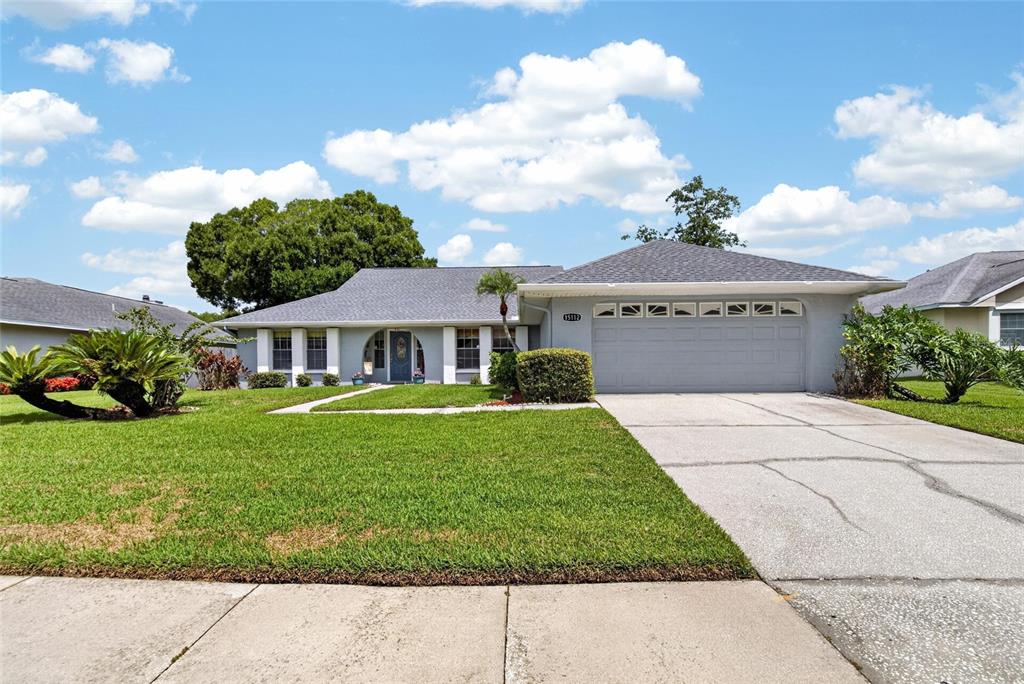 A single-story house with a gray exterior, a two-car garage, and a manicured front lawn — 15112 ROUNDUP DRIVE, TAMPA, FL