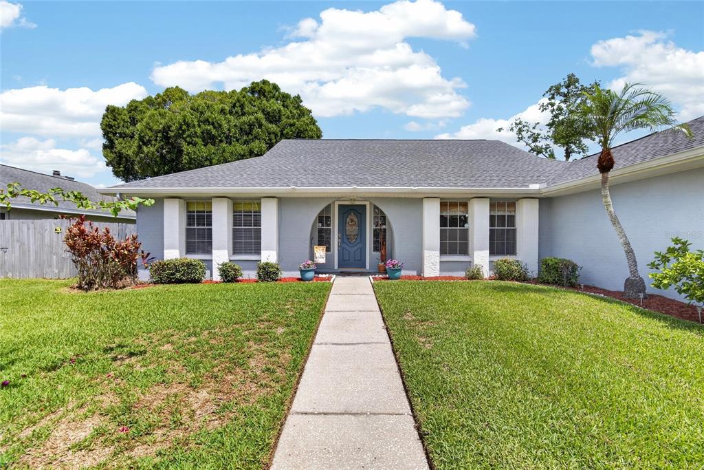 A single-story house with a gray exterior, a blue front door, and a concrete walkway — 15112 ROUNDUP DRIVE, TAMPA, FL