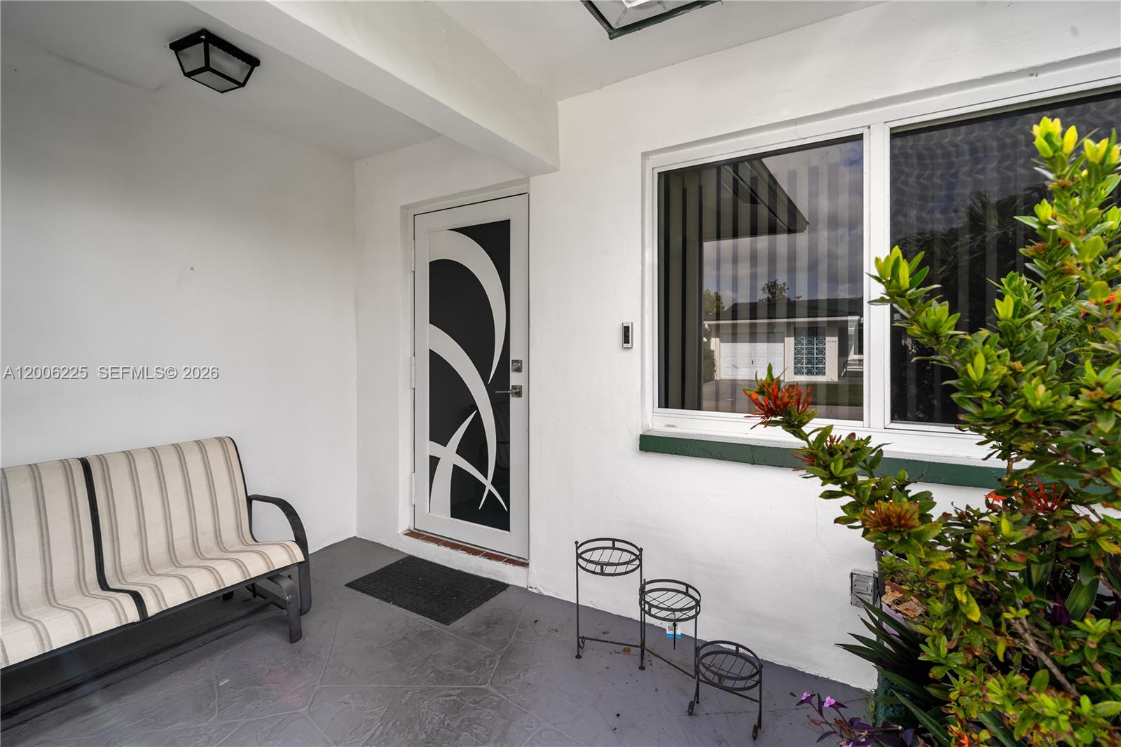 A covered porch features a striped bench, a decorative glass door, and a tiered plant stand — 4402 NW 44th Ave, Tamarac FL 33319, TAMARAC, FL