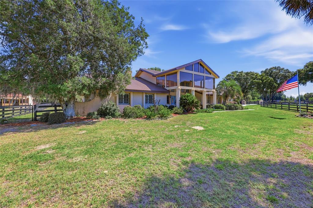 A large house with a metal roof and glass-walled facade sits on a grassy lot — 9700 SW 67TH TERRACE, OCALA, FL