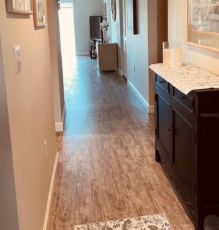 A hallway with wood-look flooring leads toward a living area featuring a dark cabinet — 9300 CLUBSIDE CIRCLE UNIT 1109, SARASOTA, FL