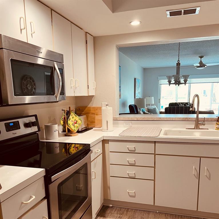 A kitchen features white cabinets, stainless steel appliances, and a pass-through window to the living area — 9300 CLUBSIDE CIRCLE UNIT 1109, SARASOTA, FL
