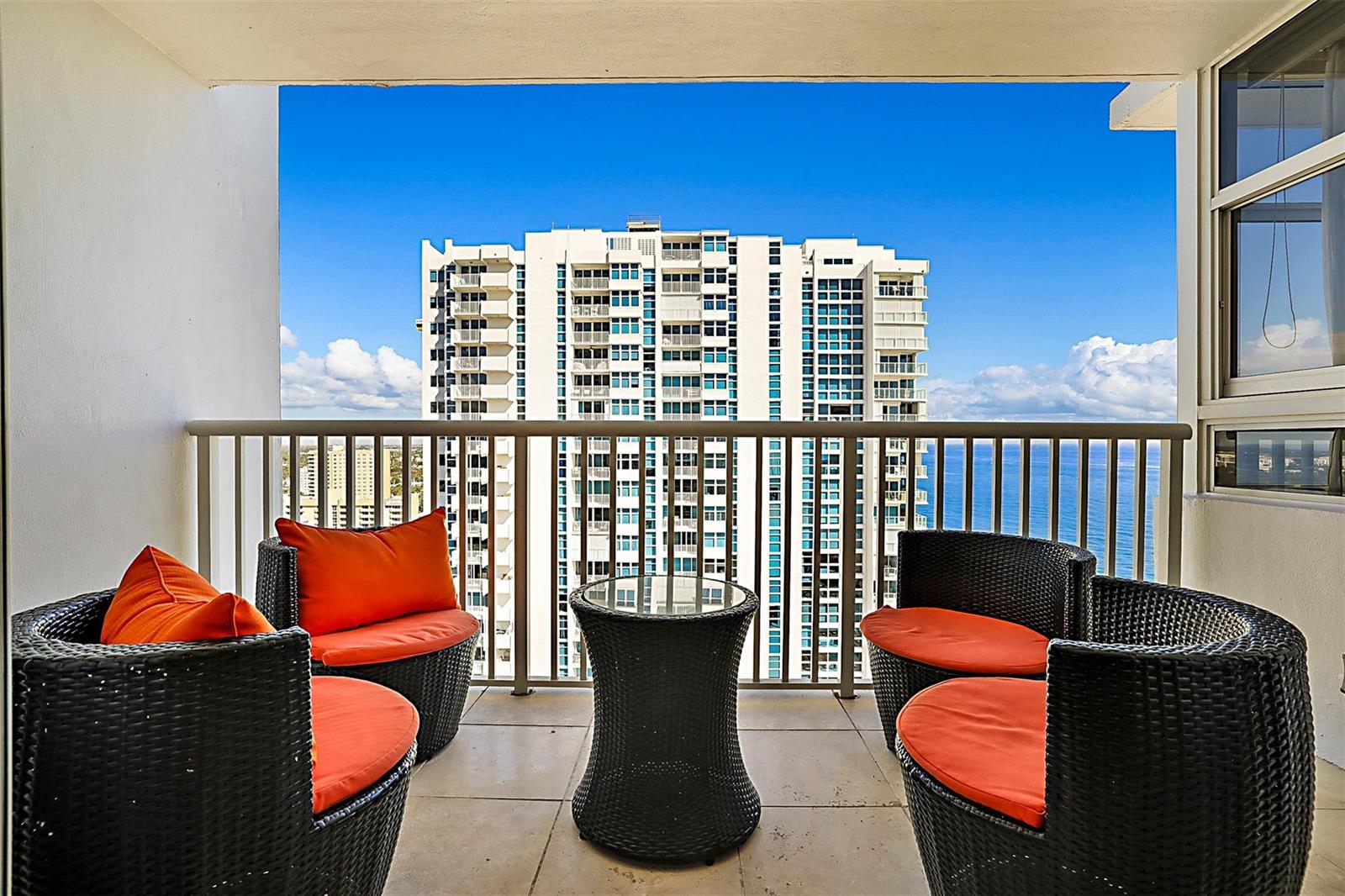 A balcony with four wicker chairs, orange cushions, and a small table overlooking the ocean — POMPANO BEACH, FL