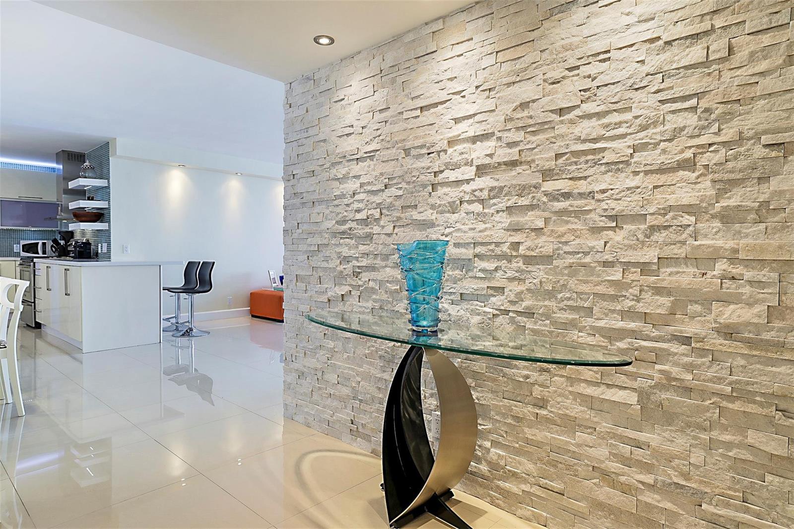 A modern interior features a textured stone accent wall and a glass-topped console table — POMPANO BEACH, FL