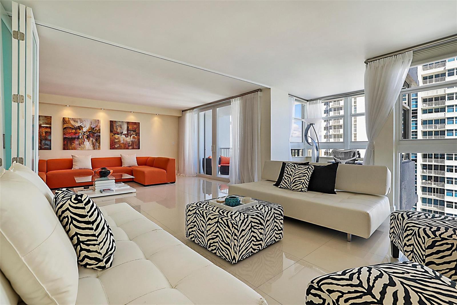 A modern living room features white leather sofas, zebra-print accents, and an orange sectional sofa — POMPANO BEACH, FL