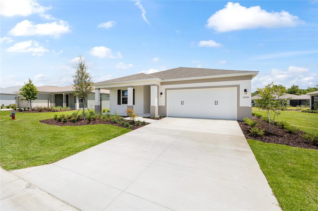 A single-story suburban house with a white garage, beige exterior, and a concrete driveway — 10355 SW 105TH TERRACE, OCALA, FL