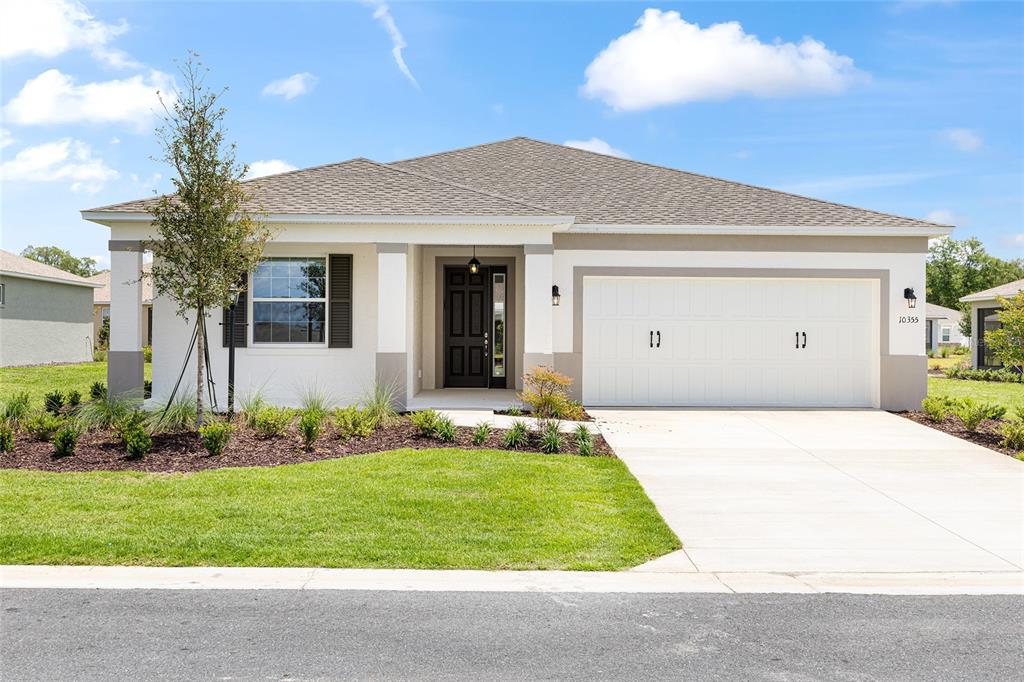 A single-story house with a white stucco exterior, dark front door, and two-car garage — 10355 SW 105TH TERRACE, OCALA, FL