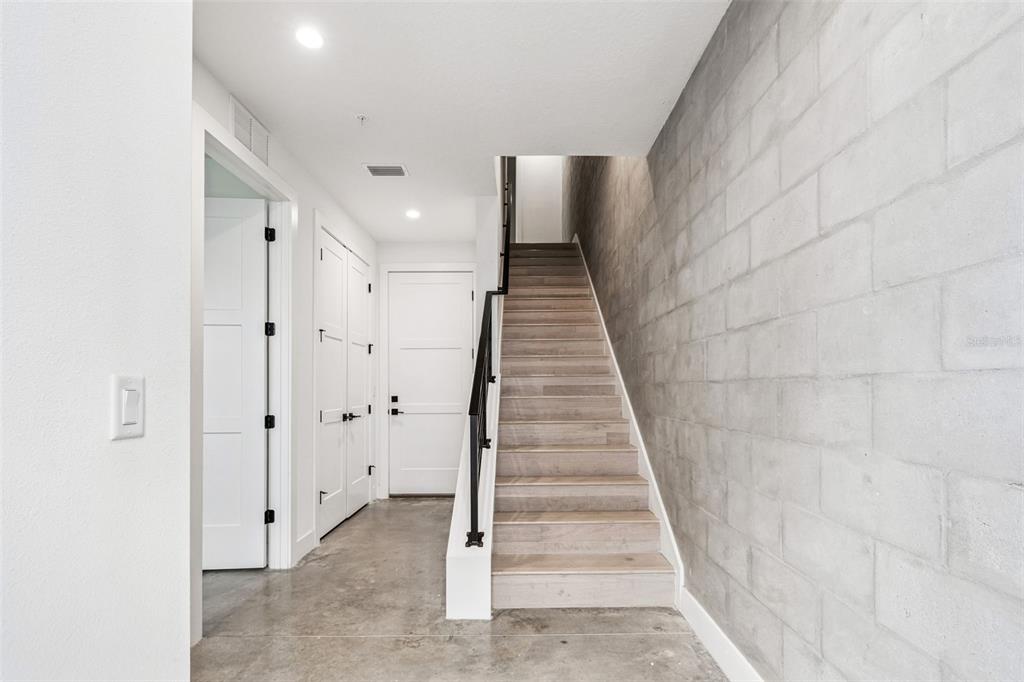 A modern entryway features a concrete block wall, wood-tread staircase, and polished concrete flooring — 2724 5TH AVENUE S, ST PETERSBURG, FL