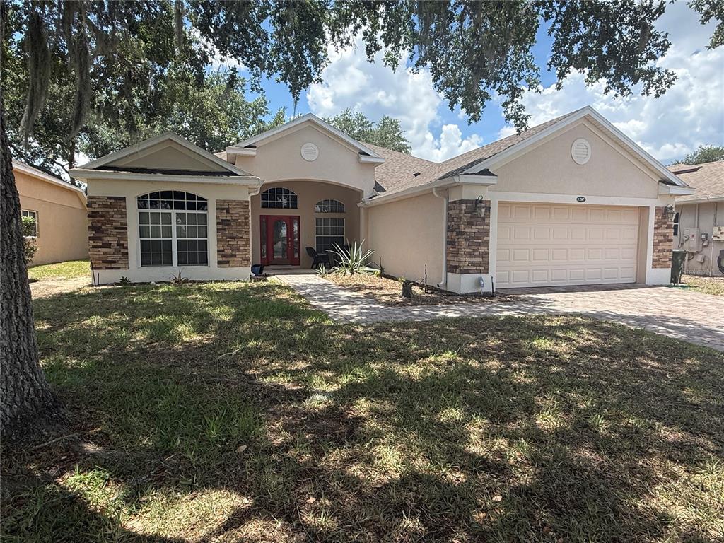 A single-story house with a beige stucco exterior, stone accents, and a two-car garage — 1287 LEGENDARY BLVD, CLERMONT, FL