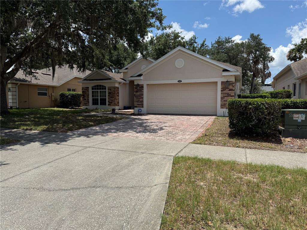 A single-story house with a beige stucco exterior, stone accents, and a two-car garage — 1287 LEGENDARY BLVD, CLERMONT, FL