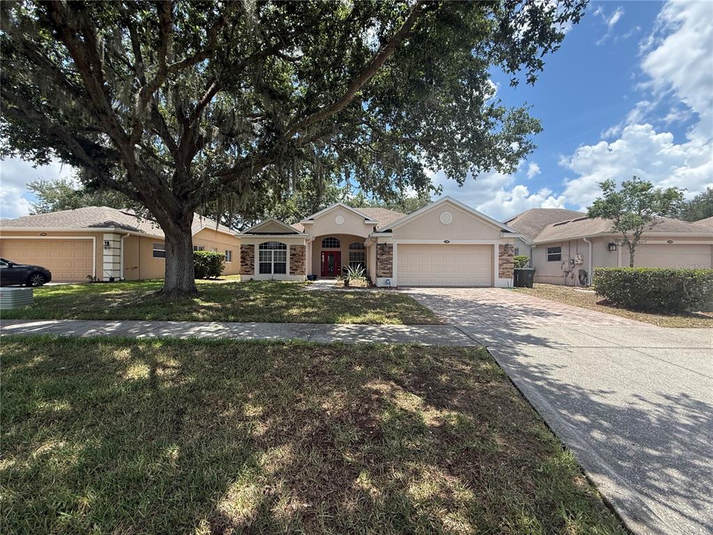 A single-story house with a beige stucco exterior, stone accents, and a two-car garage — 1287 LEGENDARY BLVD, CLERMONT, FL