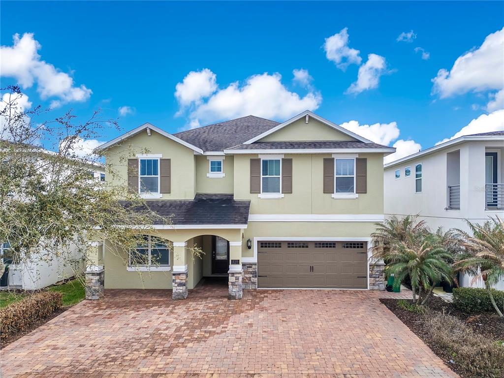 A two-story house with a light green exterior, stone pillars, and a brick paver driveway — 210 BURMA STREET, KISSIMMEE, FL