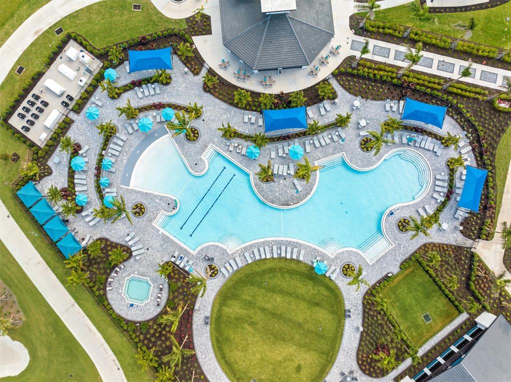 An aerial view shows a swimming pool complex with lounge chairs, umbrellas, and a clubhouse — 17625 OPAL SAND DRIVE UNIT 401, VENICE, FL