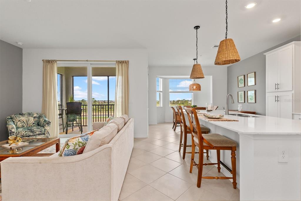 An open-concept kitchen and living area features a white island, bar stools, and sliding doors — 17625 OPAL SAND DRIVE UNIT 401, VENICE, FL