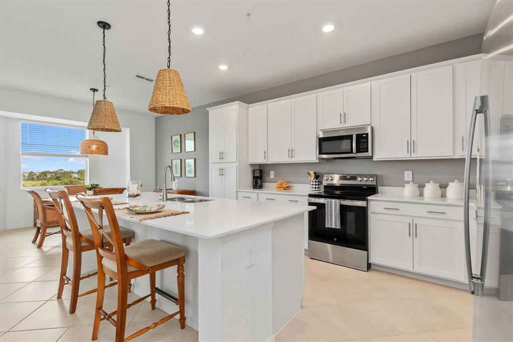 A modern kitchen features white cabinetry, a large quartz island, and stainless steel appliances — 17625 OPAL SAND DRIVE UNIT 401, VENICE, FL